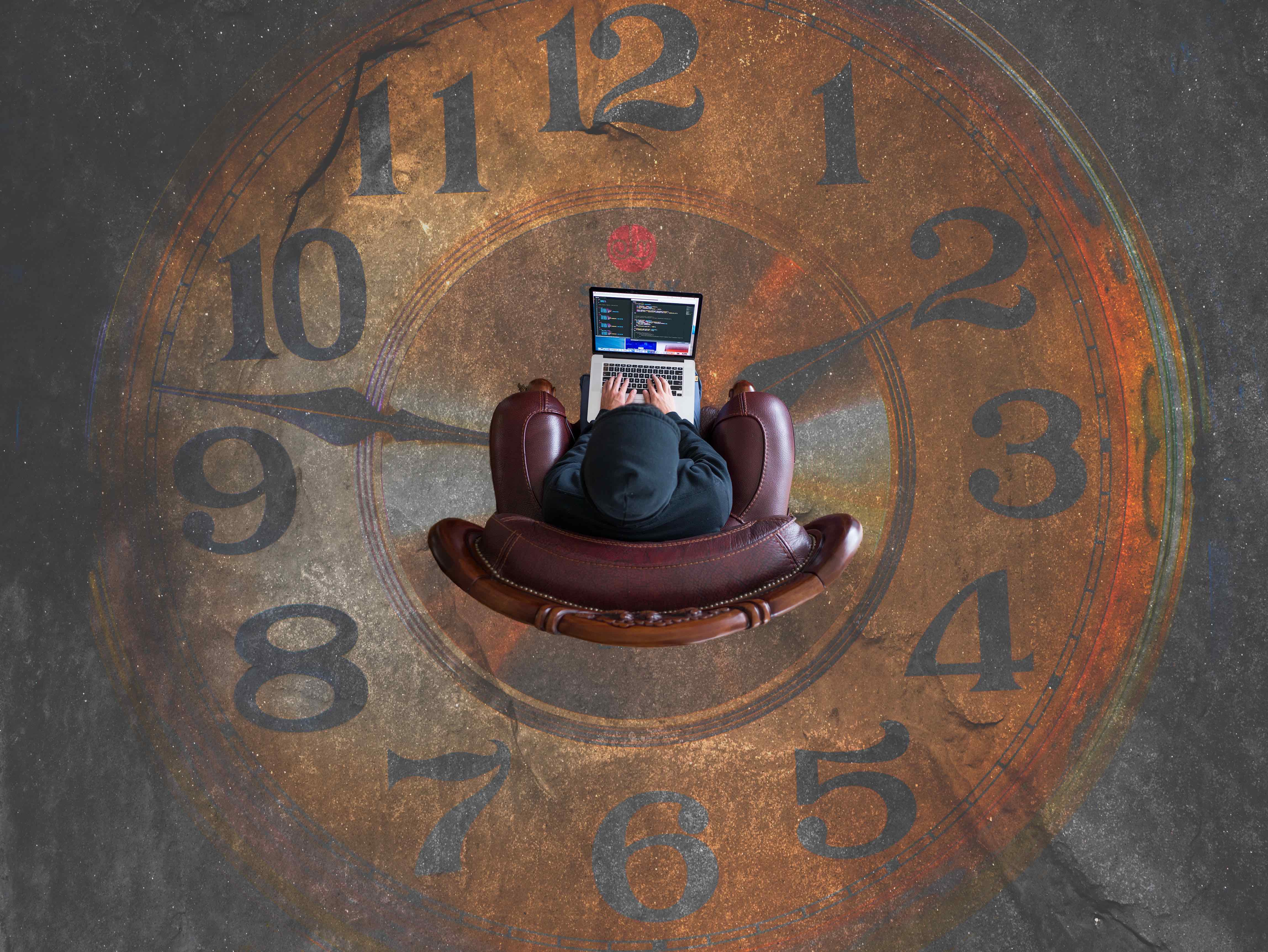 Man sitting in a chair, working on his laptop, with a painted analog clock on the floor
